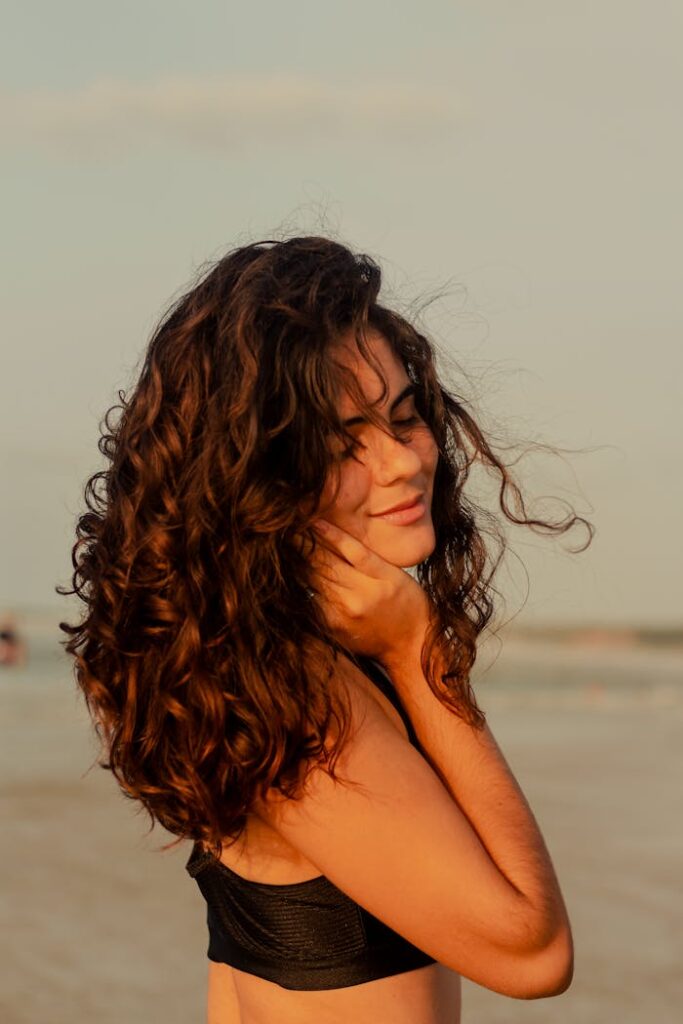 Young woman basks in the sun with curly hair and eyes closed on Maranhão's tranquil beach.