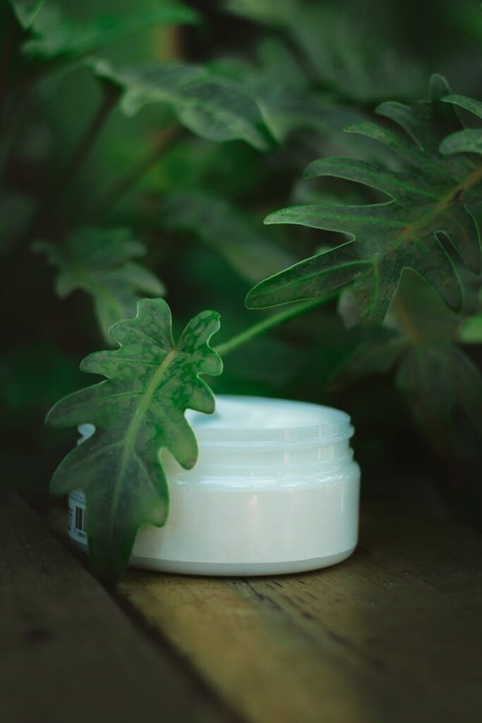 Close-up of skincare cream jar amidst lush green leaves, highlighting eco-friendly beauty.