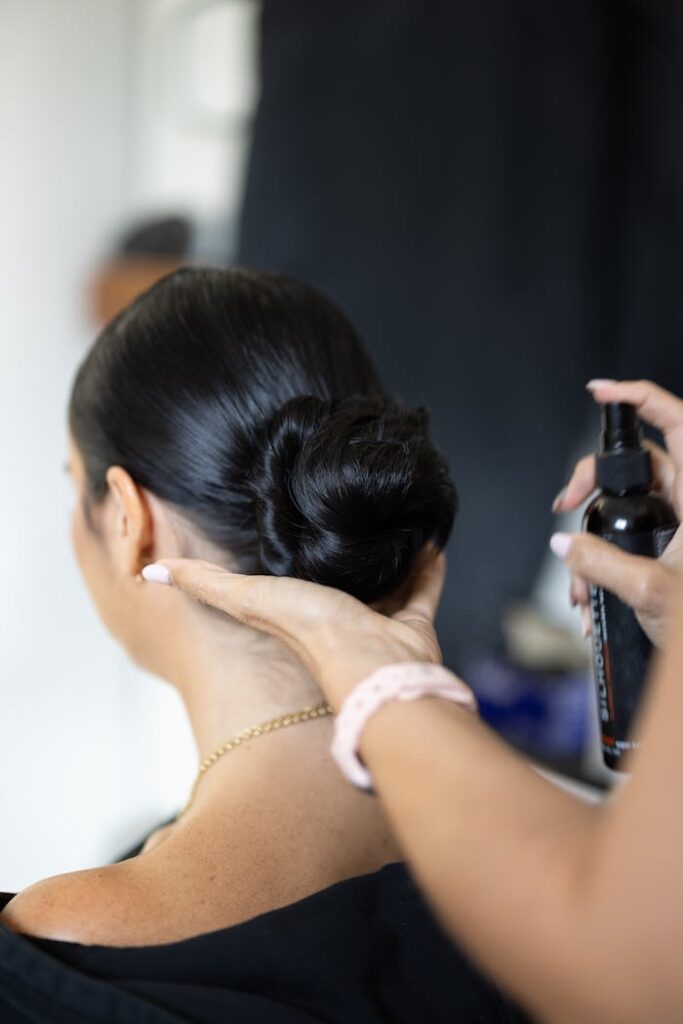 A stylist applies finishing touches to a woman's sleek updo in a professional salon.